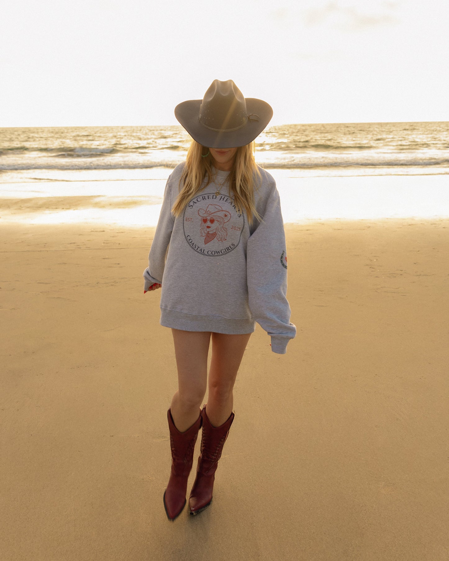 Person wearing a sweatshirt with a logo and boots on a beach