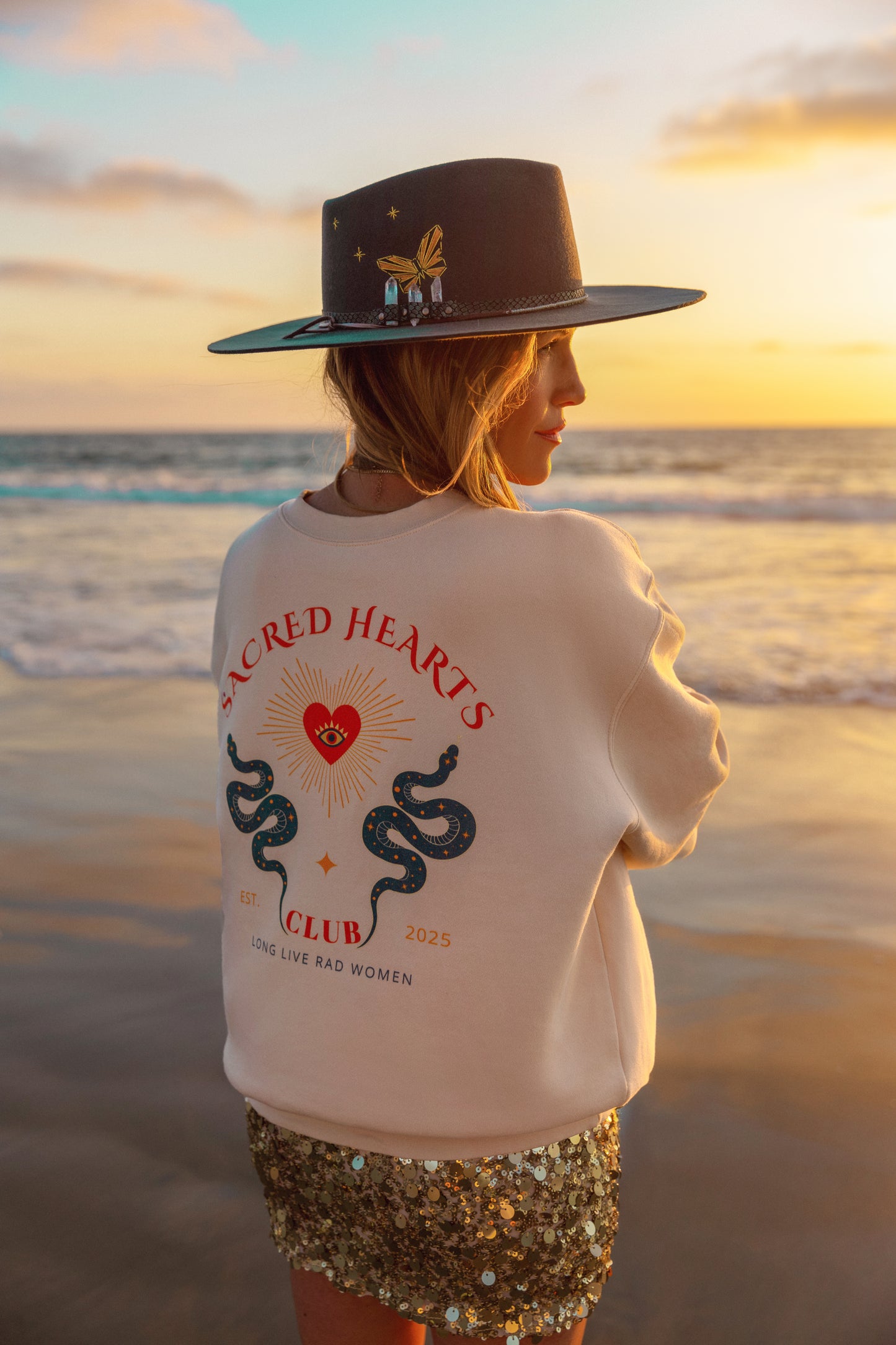 Person wearing a white sweatshirt with a design on the beach at sunset