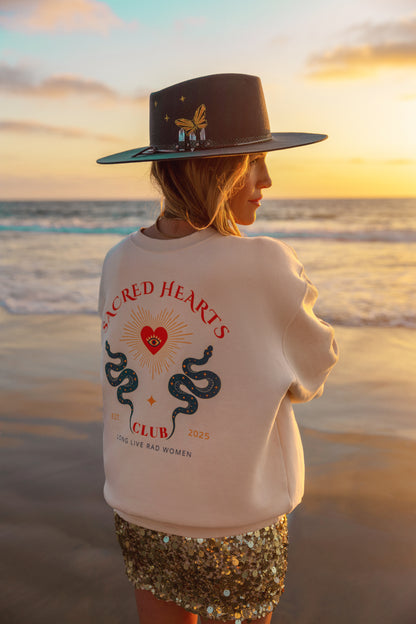 Person wearing a white sweatshirt with a design on the beach at sunset