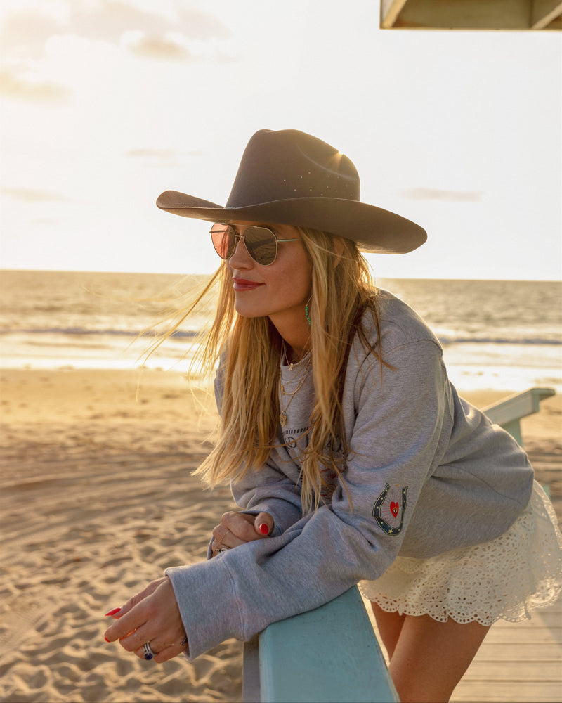 Woman on a beach wearing a hat and sunglasses with a sunset in the background
