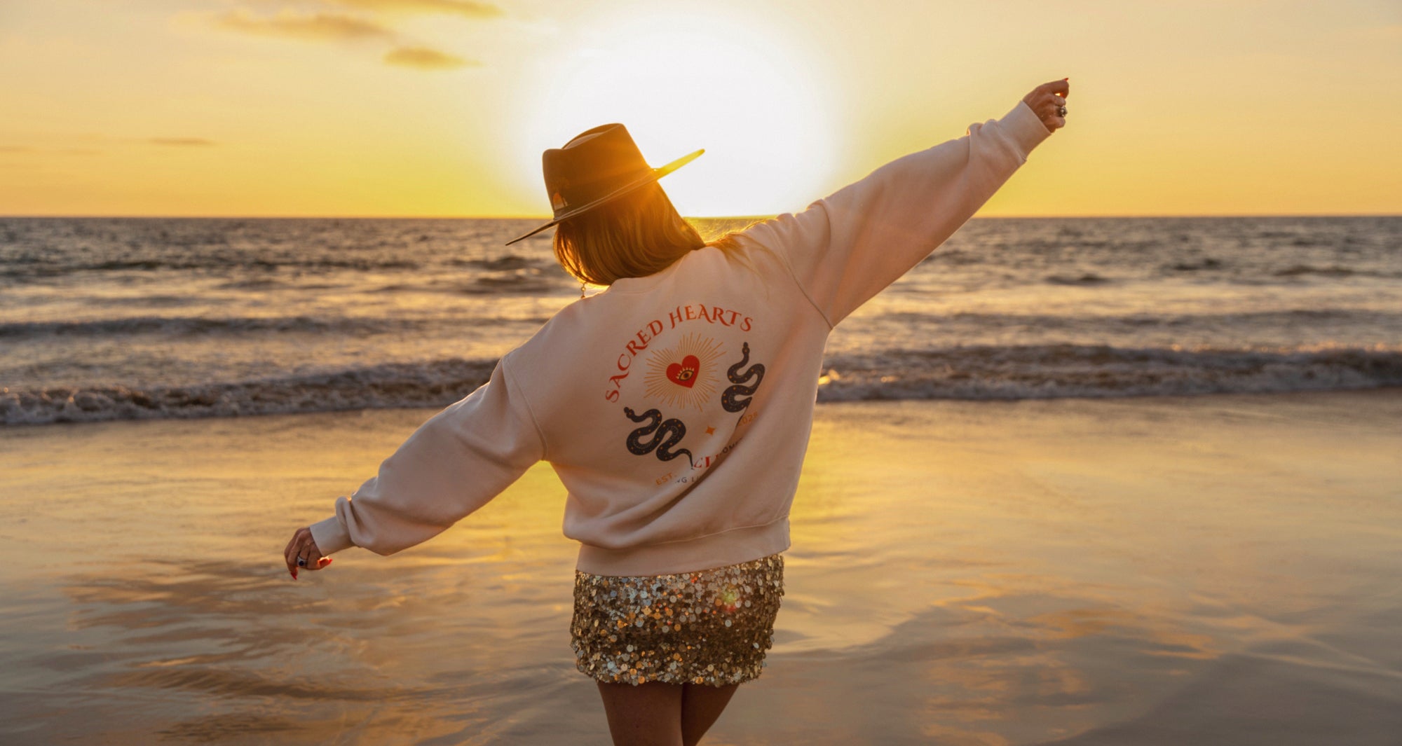 Person on a beach at sunset wearing a sweatshirt with a design and text.